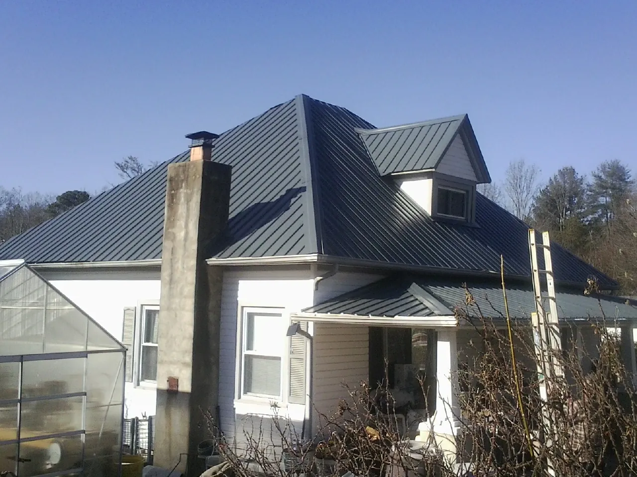 Dark blue standing seam metal roof on a white farmhouse with dormer — Slate & Tile Roof Repair by Roofing Brothers in Shubuta