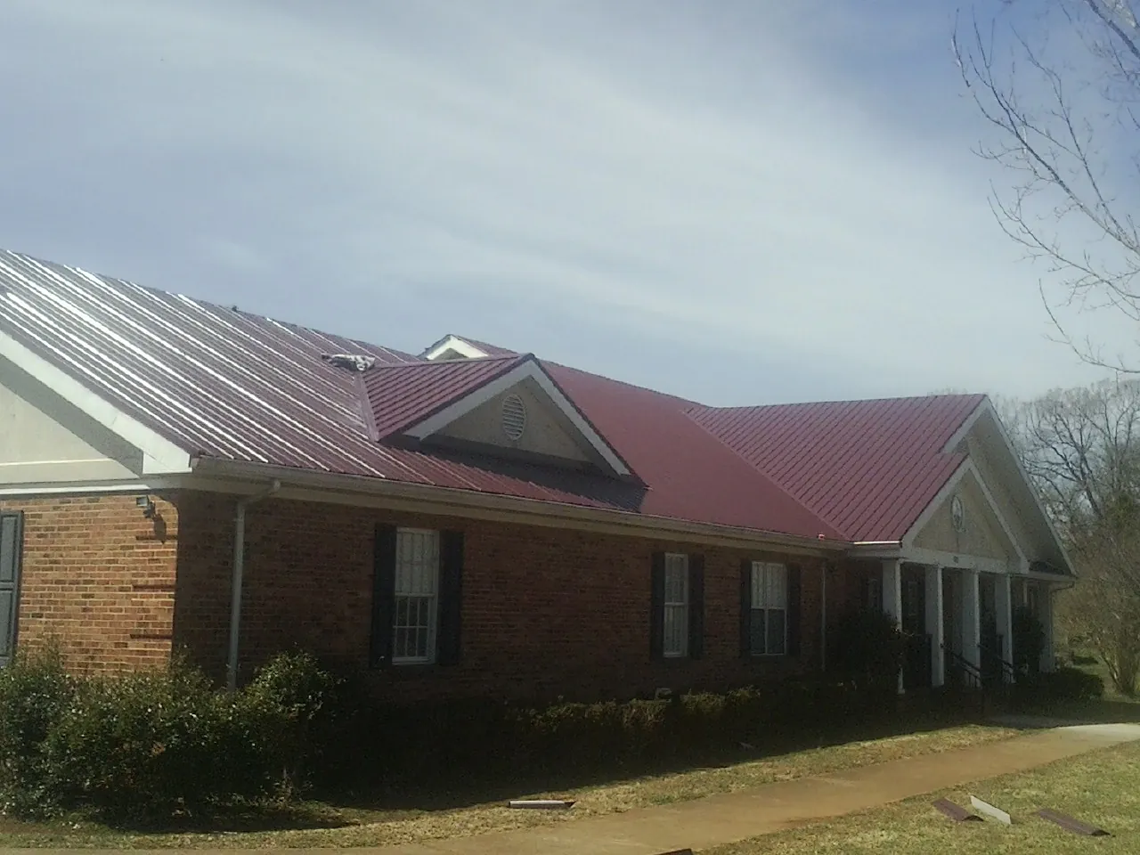 Red metal roof with gabled entries on a long brick building, from a Hail Damage Roof Repair job in Shubuta
