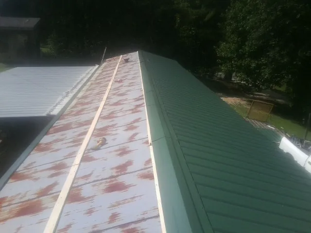 Old rusted panels beside newly installed green metal roofing — Wind Damage Roof Repair by Roofing Brothers in Shubuta