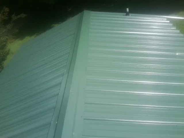 New green metal panels meeting at the ridge of a roof — Flat Roof Repair work by our crew in Shubuta