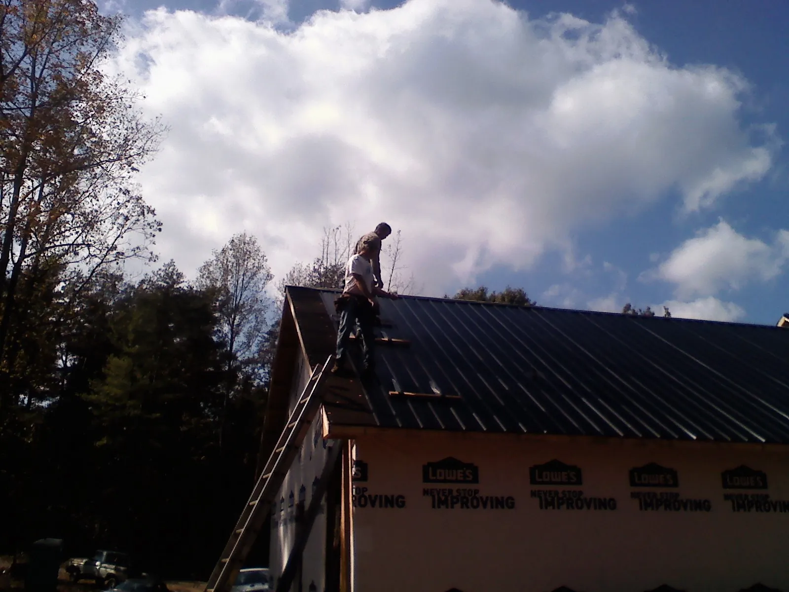Roofer fastening dark metal panels high against a cloudy sky, from a Roof Inspection job in Shubuta