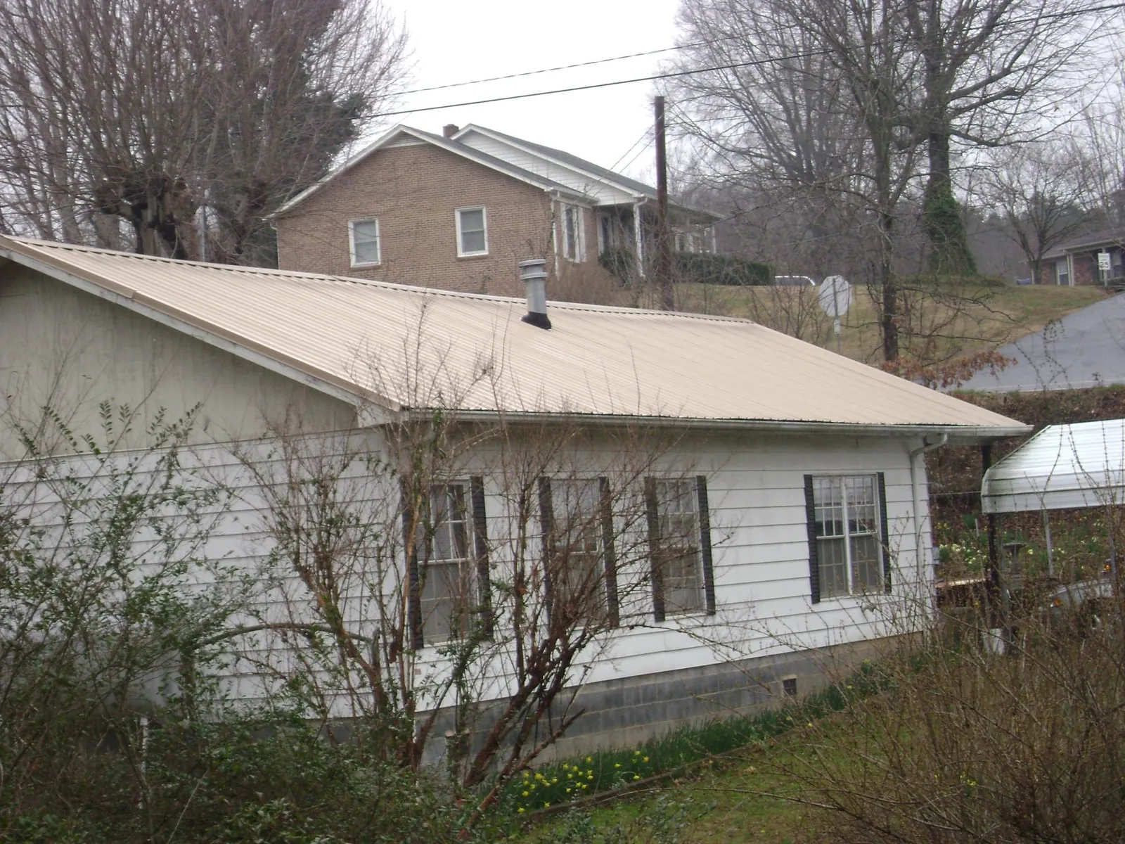 Tan metal roof on a white sided house set into a hillside — Commercial Roofing by Roofing Brothers in Shubuta