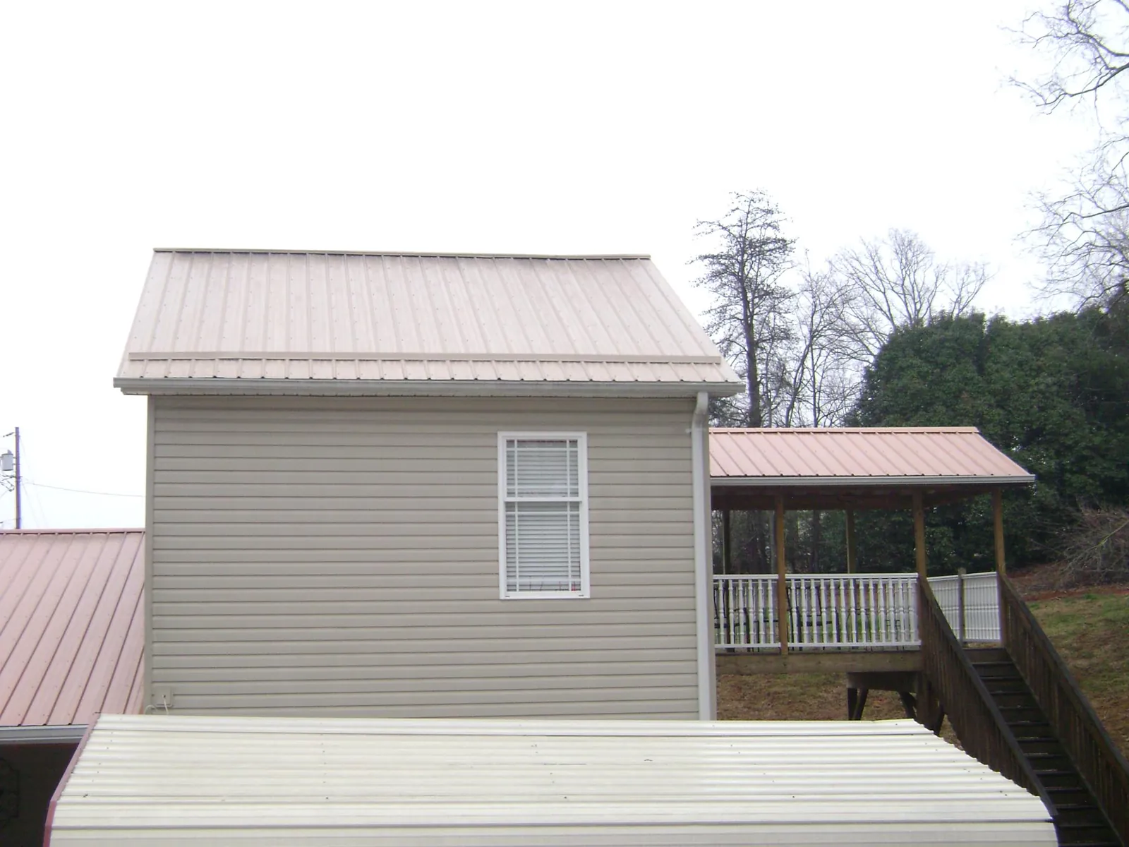 Tan metal roofs on a two story addition and attached porch, from a Roof Replacement job in Shubuta